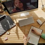 A student taking notes during a video call for online learning at home.