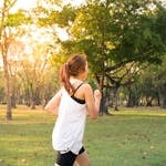 A woman jogging through a forest park in the early morning sunshine, enjoying a healthy lifestyle.